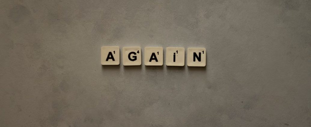 Close-up of Scrabble tiles spelling out 'Again' on a textured background.