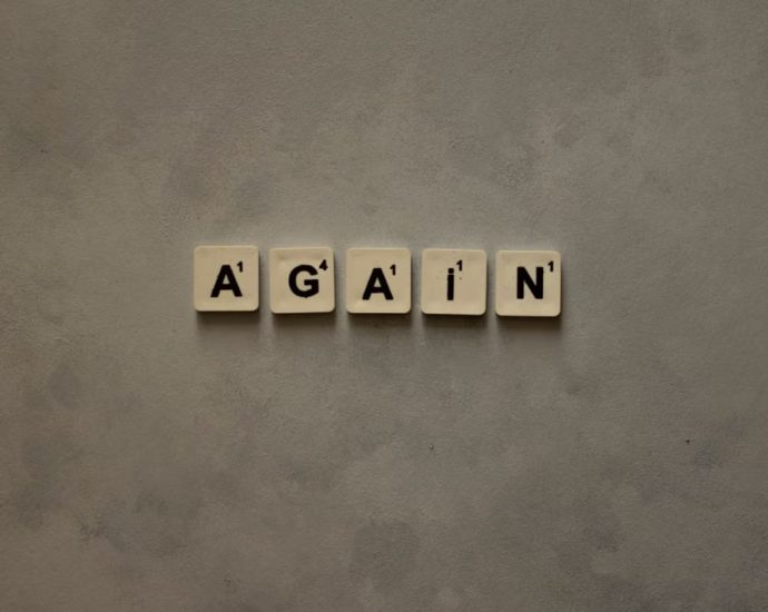 Close-up of Scrabble tiles spelling out 'Again' on a textured background.
